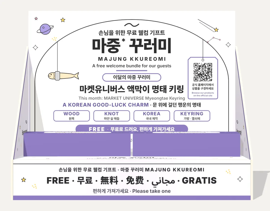마켓유니버스 매대 정면. 마켓유니버스 액막이 명태 키링 안내와 공식 홈페이지 QR이 있다.